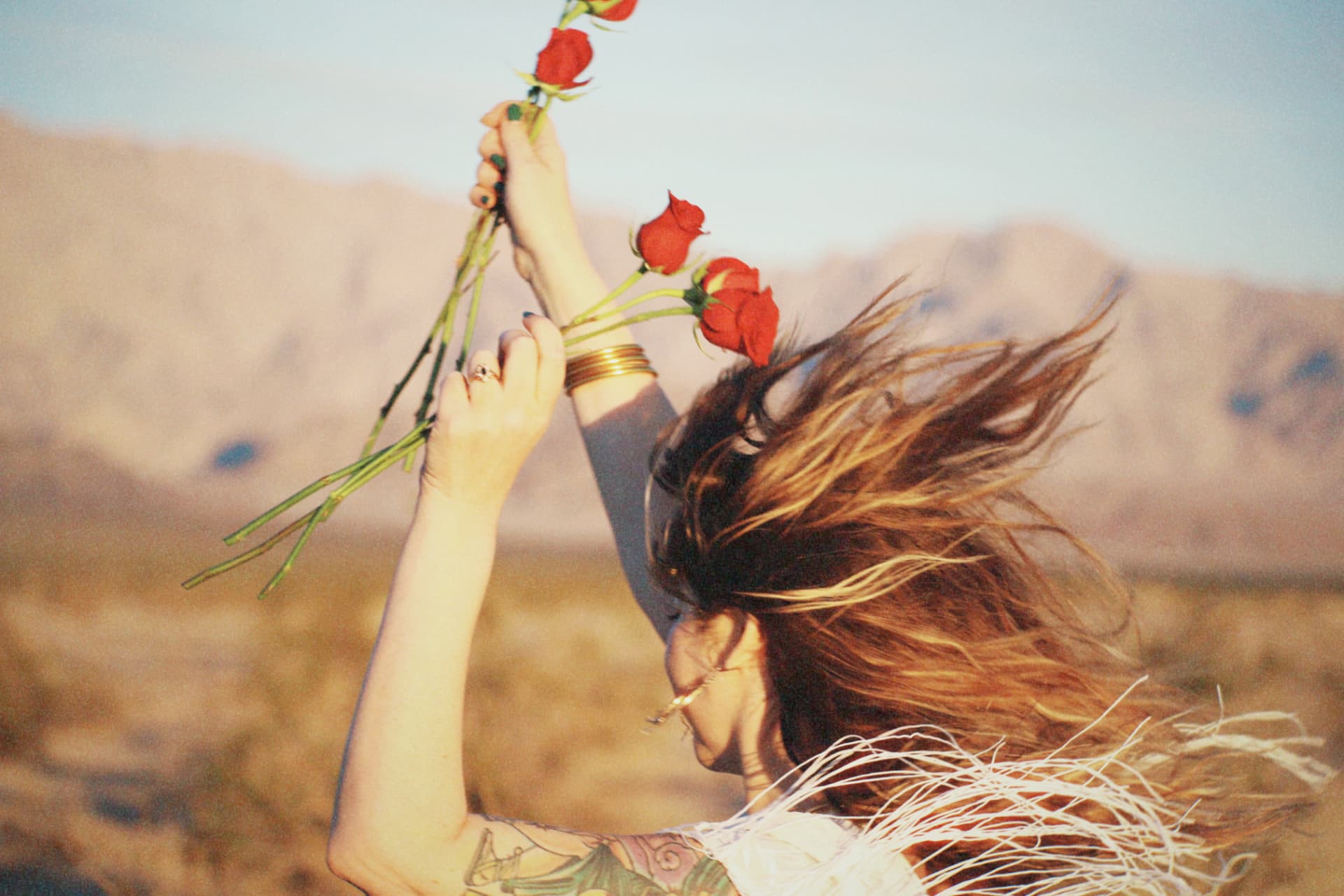 Woman holding red roses in a windswept desert landscape